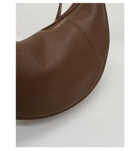 Detail view of brown pebbled leather texture and stitching on the half-moon bag
