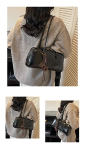 Detail of black glossy cylindrical shoulder bag with embossed letters and fringe charm