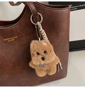Detail of plush dog keychain with TOP DOG tag on a brown leather tote bag