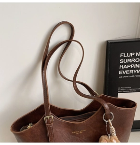 Detail of vintage brown leather tote bag showing gold logo and plush ball accessory