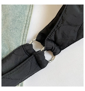 Detail eines schwarzen gesteppten Nylonriemens mit silbernen Metallringen an der Tasche