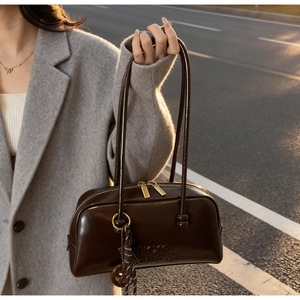 Detail of dark brown patent leather pillow bag with tassel and gold zipper in outdoor light