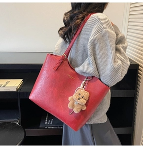 Detail of red leather tote bag with gold logo and plush bear charm on adjustable strap