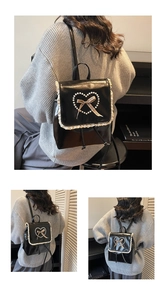 Close-up of black leather backpack featuring white lace edges and a pearl heart bow detail