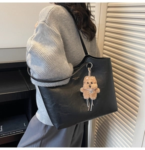 Close-up of black leather tote bag with gold lettering and brown teddy bear charm
