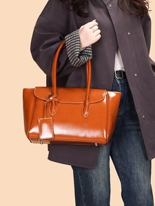Chic caramel leather tote bag with flap closure and pendant tag on female model