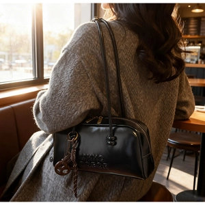 Detail of black glossy leather pillow bag with embossed letters and slim shoulder straps