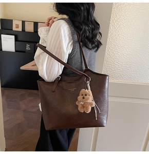 Detail of vintage brown leather tote bag with embossed text and plush bear charm