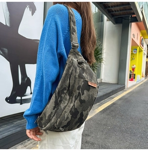 Detail of green camouflage crossbody bag with orange fashion tag and black wide strap