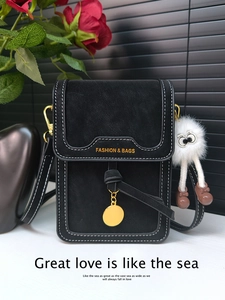 Detail of a black crossbody bag with white stitching and a cute plush monster charm