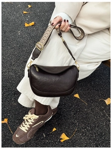 Détail du sac demi-lune marron foncé avec bandoulière jacquard sur fond de feuilles