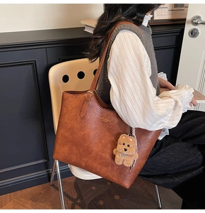 Brown vintage leather tote bag shown with a plush puppy charm on a model shoulder