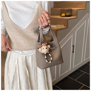 Détail d'un sac seau en cuir grainé taupe avec une texture souple et un charm ours en peluche