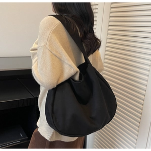 Detailed side view of a large black canvas hobo bag worn over the shoulder by a model