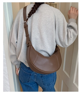 Brown moon-shaped dumpling bag made of textured faux leather on a model's shoulder