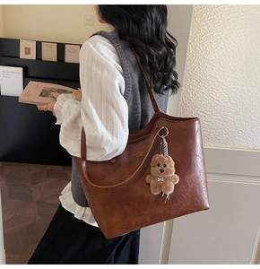 Brown vintage leather tote bag with plush bear charm shown on model in library