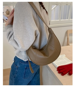 Brown half-moon crossbody bag with leather texture and knotted strap detail in lifestyle setting