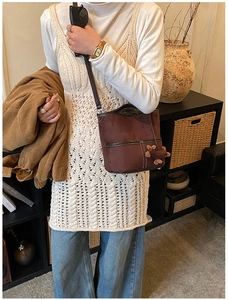 Détail du sac seau en daim marron foncé avec coutures blanches et charm d'ourson