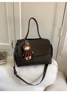 Details einer dunkelbraunen Ledertasche mit süßem Plüschbären-Anhänger und Herzpullover