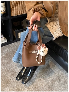 Détail du sac à main en cuir marron foncé avec fermoir rotatif et breloque ours en peluche