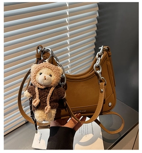 Brown half-moon hobo bag with silver chain detail and a cute teddy bear plush charm