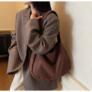 Detail of a brown suede hobo bag shown on a model in a minimalist stylish office setting