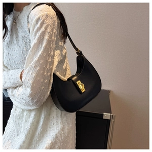Detail of a black crescent underarm bag with a polished gold metal clasp and leather strap