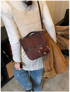 Détail du sac seau en daim marron avec surpiqûres contrastées et breloque chien