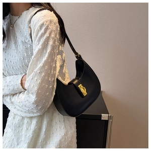 Detail view of a black hobo underarm bag with gold buckle on a white dress model