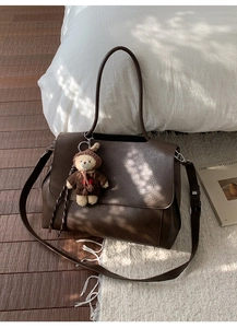 Detail der dunkelbraunen matten Kunstleder-Schultertasche mit süßem Bärenanhänger