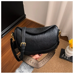 Détail du sac demi-lune en cuir noir avec ferrures dorées et bandoulière tissée colorée