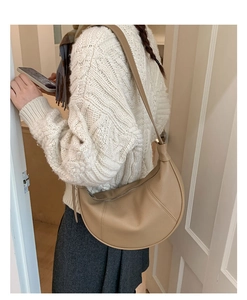Close-up of minimalist beige crescent shoulder bag with lychee grain leather on model