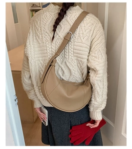 Detail view of khaki crescent bag with adjustable strap on a model wearing knit sweater
