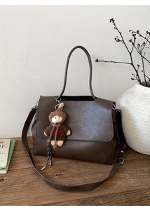 Detail der dunkelbraunen Kunstledertasche mit Vintage-Riss-Textur und einem süßen Bärenanhänger