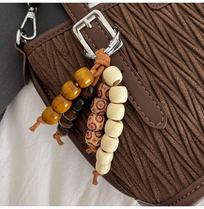 Gros plan d'un sac seau plissé marron avec pendentif en perles de bois et boucle argentée