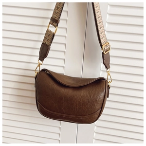 Détail du sac besace en cuir marron avec bandoulière tissée et finitions dorées