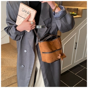 Détail du sac seau en daim marron avec garniture en cuir contrasté et charme d'ours en peluche