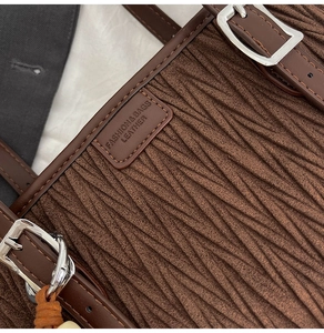 Détail de sac seau marron foncé avec texture tissée, finitions cuir et boucle argentée