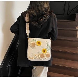 Detailed close-up of a cream crossbody bag with sunflower embroidery and woven strap