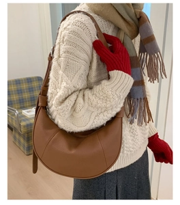 Brown leather crescent hobo bag styled with a white knitted sweater in a cozy indoor setting