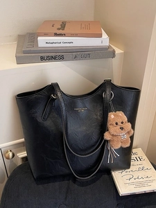 Large black pebbled leather tote bag with gold lettering and plush puppy charm decor