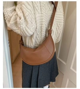 Close-up of a brown lychee-patterned half-moon crossbody bag styled with a white sweater