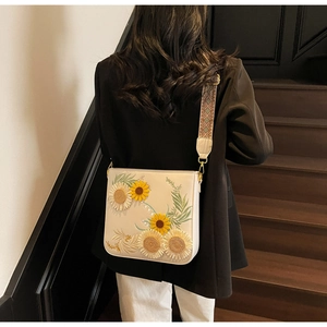 Detail of white leather shoulder bag featuring sunflower embroidery and jacquard strap