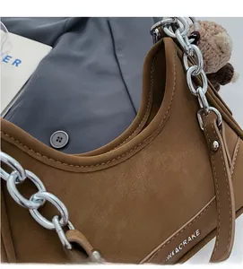 Detail of brown textured leather bag with silver chain strap and cute crochet bear charm