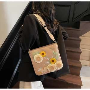 Detail of sunflower and daisy embroidery on a beige crossbody bag with woven strap