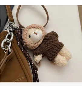 Close-up of a brown knitted bear charm with a hoodie attached to a leather handbag