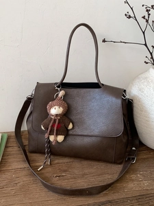 Braune Vintage-Ledertasche mit Teddybär-Anhänger auf einer rustikalen Holzoberfläche