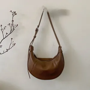 Detailed macro of brown lychee texture leather crescent bag with adjustable silver buckle