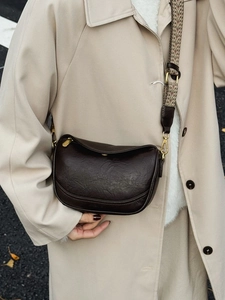 Sac lune marron foncé chic avec bandoulière tissée porté par un mannequin en décor d'automne