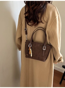 Détail du sac seau plissé marron café avec pompon en perles et étiquette de mode